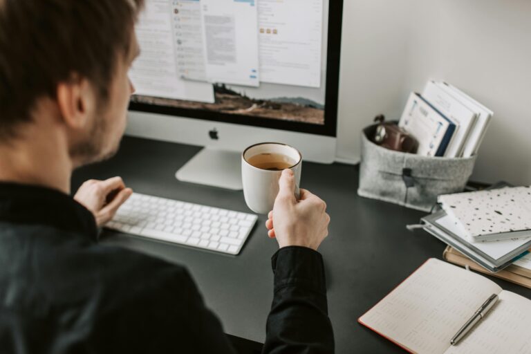 A man enjoying coffee while working on a computer indoors. Ideal for work-from-home scenarios.